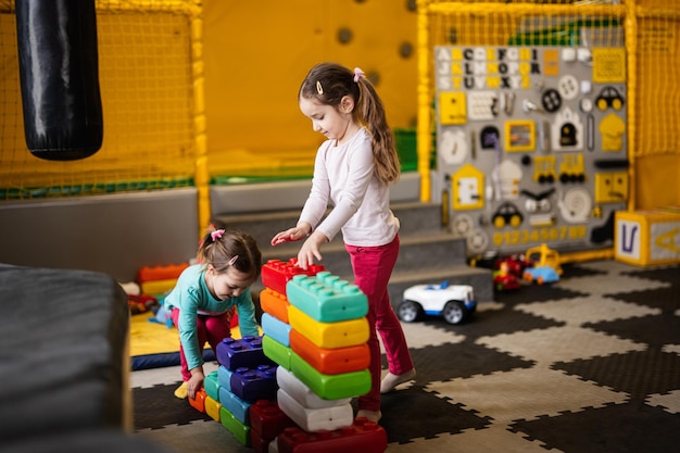 Duas irmãs brincando no centro infantil enquanto constroem com blocos de plástico coloridos