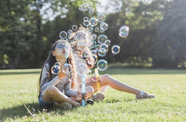 Foto duas irmãs caucasianas soprando muitas bolhas de sabão enquanto estavam sentadas no parque