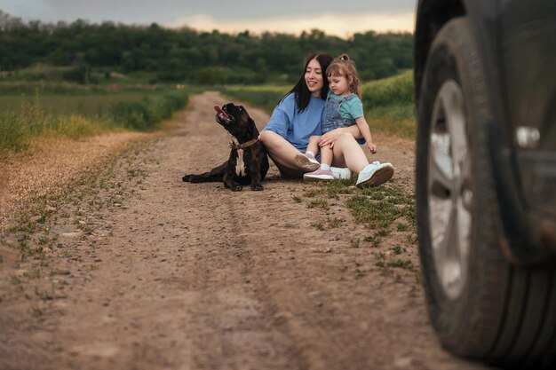 Duas irmãs de diferentes idades no verão em uma caminhada sentam-se em uma estrada rural com seu cachorro