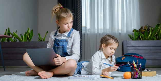 Duas irmãs, deitado no chão na sala de estar usando laptop, tocando e desenhando