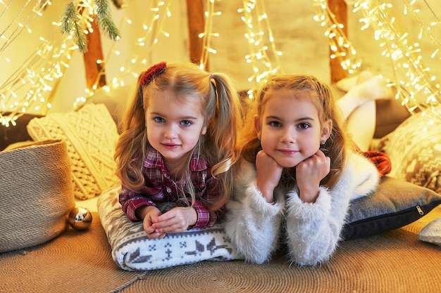 Duas irmãs do bebê meninas na árvore de Natal do fundo. Família feliz. Conceito de amizade
