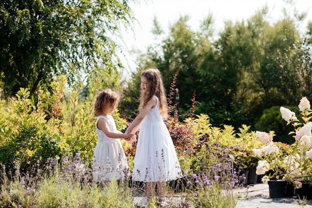 Duas irmãs em vestidos brancos dançando ao ar livre no mercado de flores Garotas felizes de mãos dadas entre vasos de flores e plantas