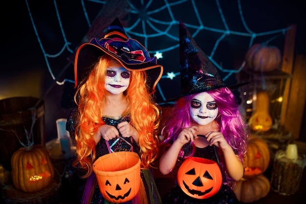 Duas irmãs engraçadas fofas celebram o feriado. Crianças alegres em fantasias de carnaval prontas para o Halloween em decorações de halloween