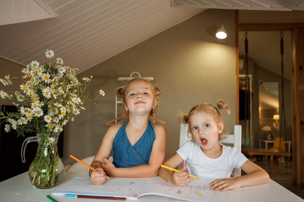 Duas irmãs engraçadas passando tempo juntas desenhando em seu caderno com seus lápis em casa dentro de casa