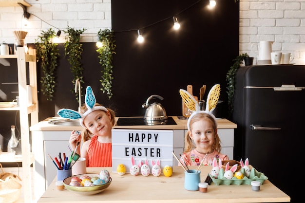 Duas irmãs estão se divertindo enquanto decoram ovos de páscoa na cozinha feliz páscoa parabéns