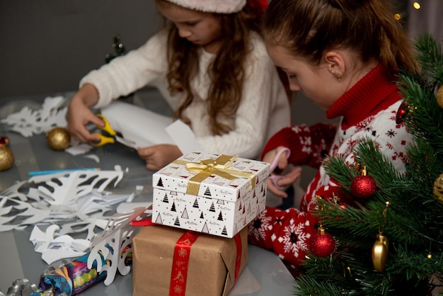 Duas irmãs fofas cortam flocos de neve de papel se preparando para o feriado de Ano Novo Natal Conforto