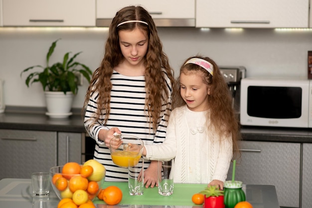 Duas irmãs fofas estão fazendo suco de laranja fresco.