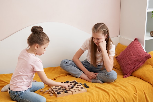 Duas irmãs jogando damas em um mau se divertindo em casa, conceito de crianças felizes