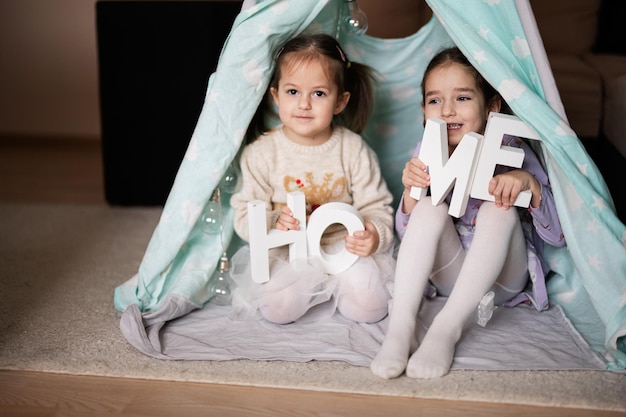 Duas irmãs meninas na tenda wigwam com cartas caseiras de madeira