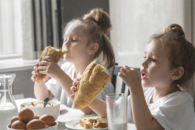 duas irmãs meninas tomam café da manhã em casa de manhã na cozinha