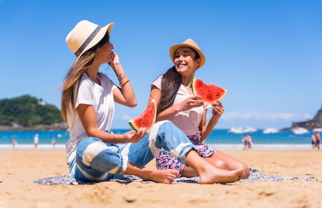 Duas irmãs no verão na praia comendo uma melancia curtindo as férias com o mar ao fundo