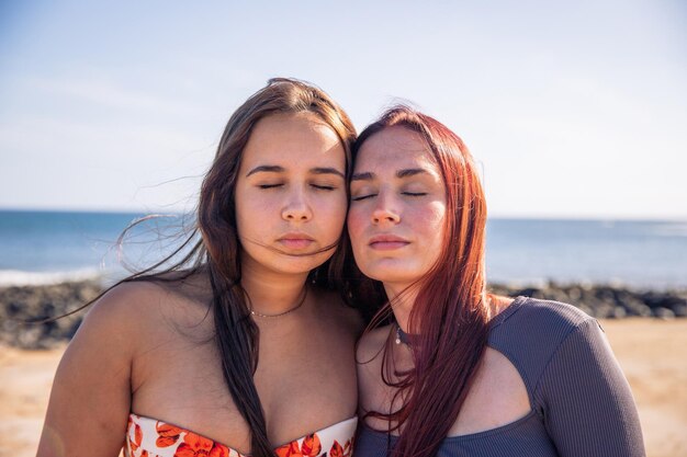 Duas irmãs posam com rostos próximos e olhos fechados na praia amor entre irmãs