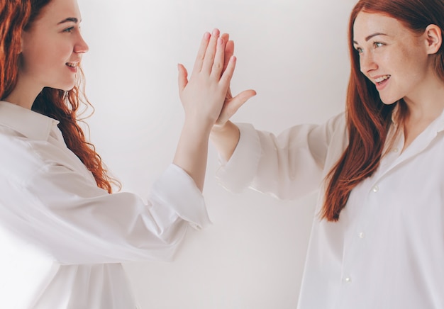 Duas irmãs ruivos estão isoladas em um fundo branco em camisas grandes e espaçosas. Duas meninas se cumprimentam.