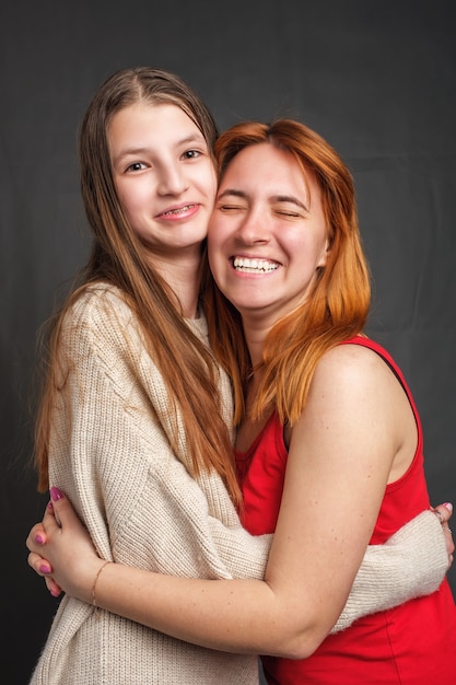 Duas irmãs sorridentes abraçadas dentro de casa e olhando para a frente