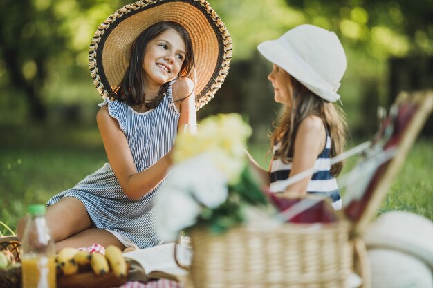 Duas irmãs sorridentes bonitas bebendo suco de laranja na natureza e curtindo um dia de piquenique.