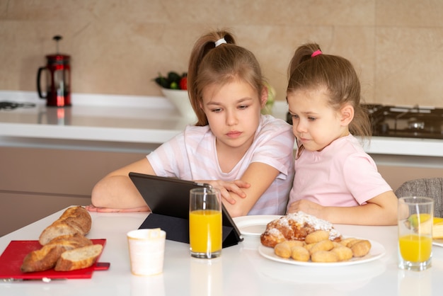 Duas irmãs tomando café e assistindo desenhos animados sobre tablet juntos, o conceito de família feliz