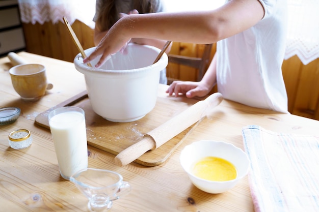 Duas irmãzinhas com as mãos bagunçadas na farinha fazem massa de cozimento na mesa de madeira na cozinha Tábua de corterolling pintowelkoilAtividade doméstica familiar com criançasConceito de padaria culinária