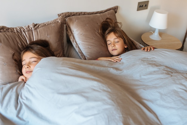 Duas irmãzinhas dormindo na cama em casa