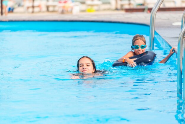 Duas irmãzinhas estão nadando em uma grande piscina com água azul clara minha, perto do hotel, no fundo do mar e da praia. Conceito de férias tropical quente com crianças