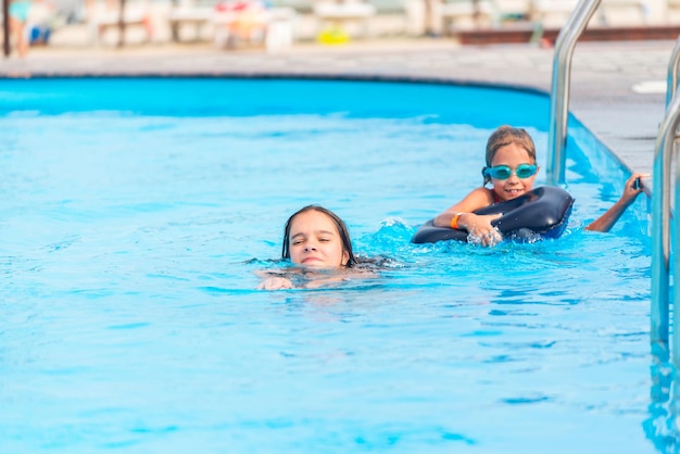 Duas irmãzinhas estão nadando em uma grande piscina com água azul clara minha, perto do hotel, no fundo do mar e da praia. Conceito de férias tropical quente país com crianças