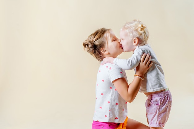 Duas irmãzinhas se abraçam e se beijam sobre um fundo claro. o conceito de uma família feliz, parentalidade, amor fraternal