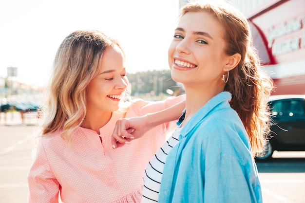 Duas jovem e bela mulher hipster sorridente em roupas e vestidos da moda de verãoMulheres despreocupadas sexy posando no fundo da rua Modelos puros positivos se divertindo no pôr do sol abraçando e enlouquecendo