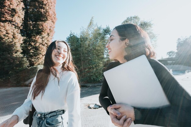 Duas jovem estudante indo para a aula enquanto conversava e ria ao ar livre da faculdade durante um dia brilhante. estudos universitários, trabalhos universitários, estilo moderno. preparando uma apresentação para a aula.