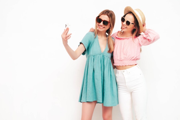 Duas jovem linda morena sorridente hipster em vestidos de verão da moda Mulheres despreocupadas sensuais posando perto da parede branca Modelos positivos se divertindo Alegre e feliz tirando fotos de selfie