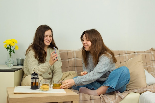 Duas jovens alegres bebem chá e usam um telefone celular se comunicam sobre tópicos positivos