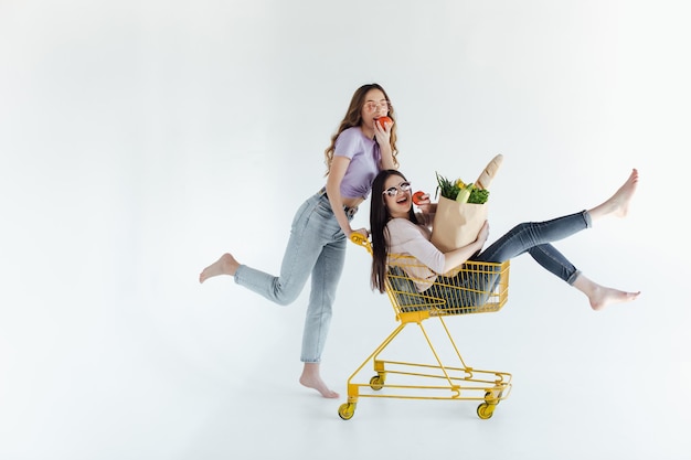 Duas jovens alegres em roupas coloridas da moda sorrindo e se divertindo com carrinho