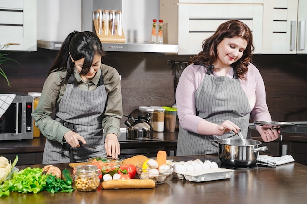 Foto duas jovens amigas alegres preparando a refeição juntas na cozinha de casa.