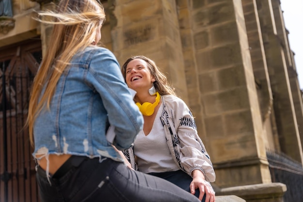 Duas jovens amigas caucasianas na cidade junto com um livro sentado ao lado de uma igreja aproveitando o fim de semana da primavera