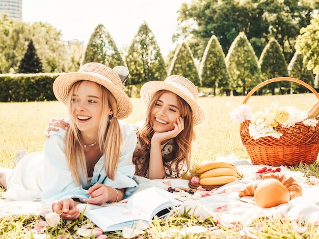 Duas jovens belas garotas hippie sorridentes em vestido de verão da moda e chapéus. Mulheres despreocupadas fazendo piquenique do lado de fora.