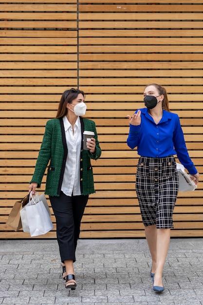 Duas jovens caminhando pela rua usando máscaras e conversando alegremente após as compras