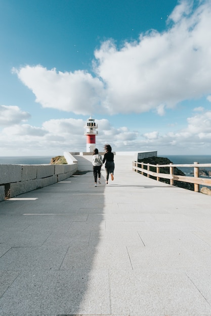 Duas jovens correndo em direção a um farol vermelho e branco