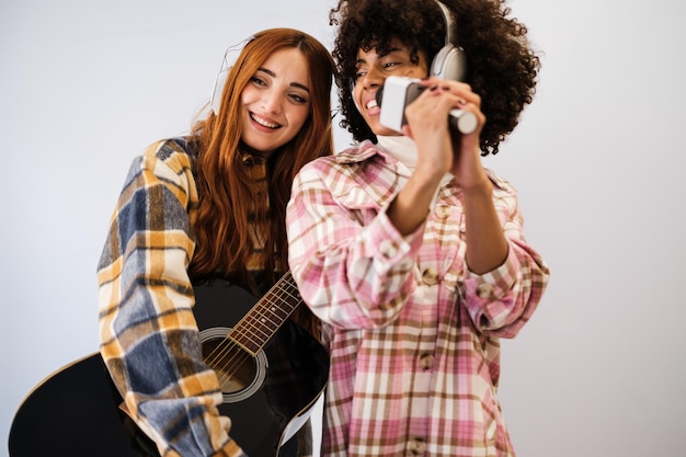 Foto duas jovens de diferentes etnias cantando e tocando música em casa juntas e improvisando karaokê de estilo de vida de criação musical de conceito