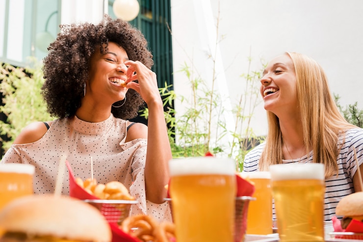 Foto duas jovens desfrutando de um lanche e uma cerveja juntas