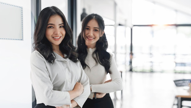 Duas jovens empresárias asiáticas felizes parecendo confiantes em pé no espaço de cópia de escritório moderno