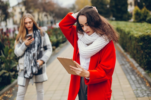 Duas jovens empresárias elegantes em pé em uma cidade de outono e usam o tablet