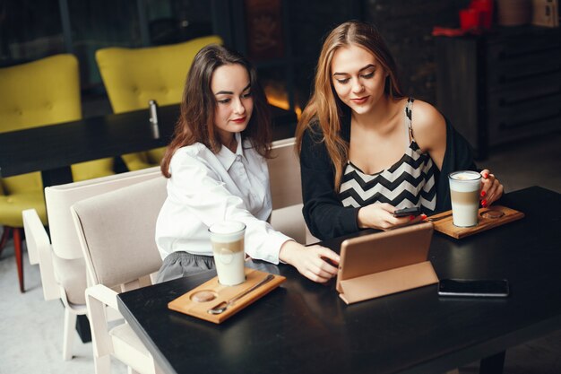 Duas jovens empresárias elegantes sentado em um café e usar o tablet