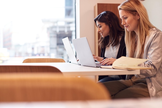 Duas jovens empresárias em reunião ao redor da mesa no espaço de trabalho moderno em plano aberto