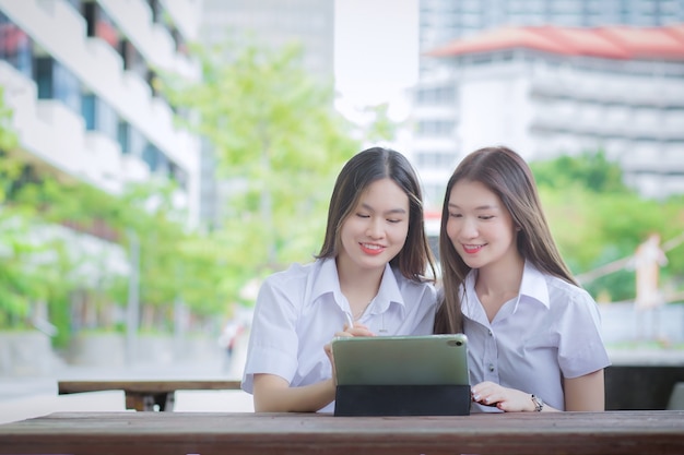 Duas jovens estudantes asiáticas estão se consultando e usando um tablet para pesquisar informações