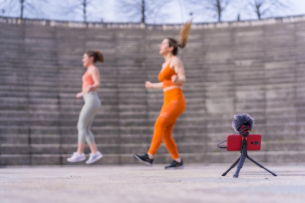 Duas jovens fitness em um parque da cidade gravando a aula com o telefone para os seguidores das redes sociais