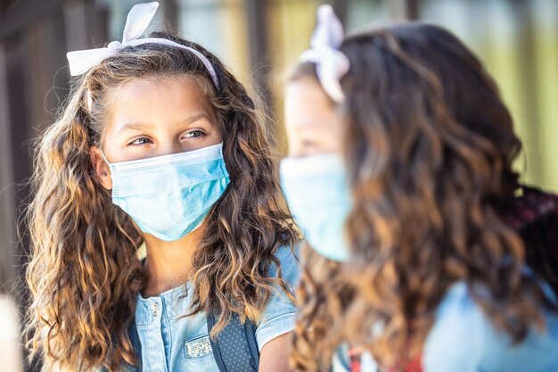 Foto duas jovens irmãs gêmeas colegas de classe com máscaras conversam a caminho da escola durante a quarentena de covid-19.