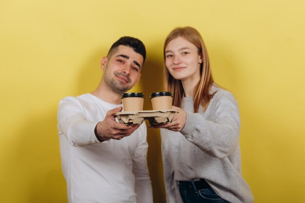 Duas jovens lindas garota e cara de pé em um fundo amarelo Eles bebem café