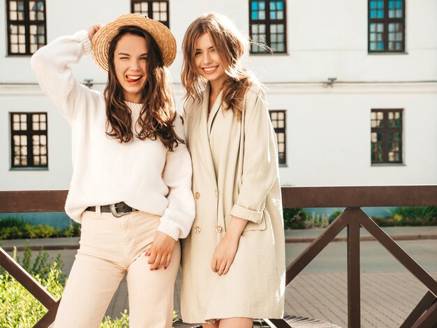 Duas jovens lindas sorrindo hipster feminina com casaco e suéter branco da moda