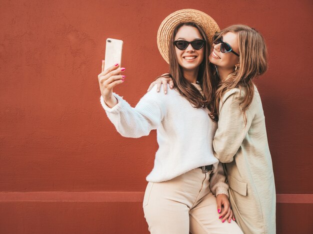 Duas jovens lindas sorrindo hipster feminina com casaco e suéter branco da moda