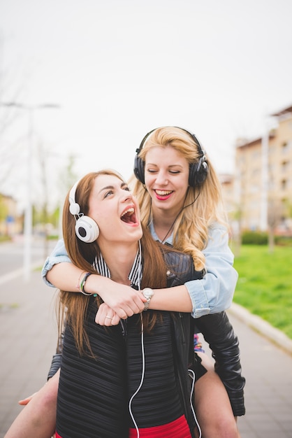 Duas jovens loiras e morenas meninas ouvindo música na cidade