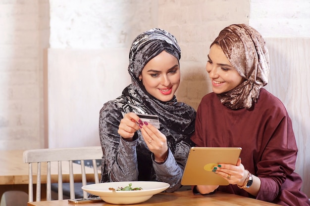 Duas jovens muçulmanas bonitas conversam e compram on-line usando um tablet eletrônico