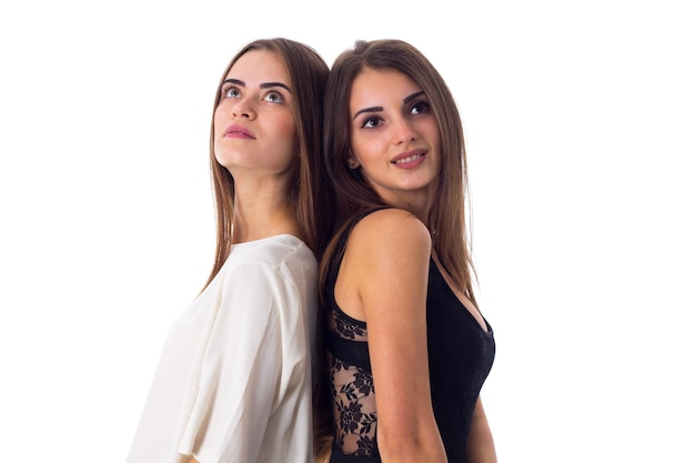 Duas jovens mulheres bonitas em camisas brancas e pretas em pé de costas em fundo branco no estúdio